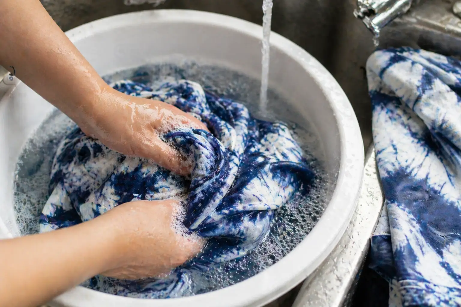 Hands washing blue tie dye fabric in cold water
